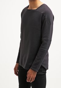 Sudadera de manga larga gris oscuro con un ajuste relajado, cuello redondeado y mangas raglán. Tejido suave con textura lisa y costura mínima.
