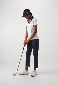 Balta golfo polo marškinėliai su tamsiai mėlynomis detalėmis, tamsiai mėlynos trumpintos kelnės ir balti golfo batai. Dėvimas tamsiai mėlynas vizierius. Žaidėjas laiko golfo klubą.