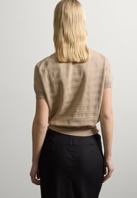 Gebreide beige top met korte mouwen en geribbelde zoom, gecombineerd met een zwarte rok. De stof lijkt zacht met een subtiele textuur en een losse pasvorm.