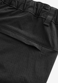 Shorts de tela negra con cinturilla elástica, textura suave y detalle de bolsillo oculto. Patrón de cuadrícula sutilmente visible.