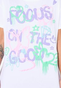 Hvid bomulds t-shirt med multicolore graffiti-stil grafik, herunder en sommerfugl, stjerner, hjerter og en diamant i pastelfarver som pink, grøn og lilla.