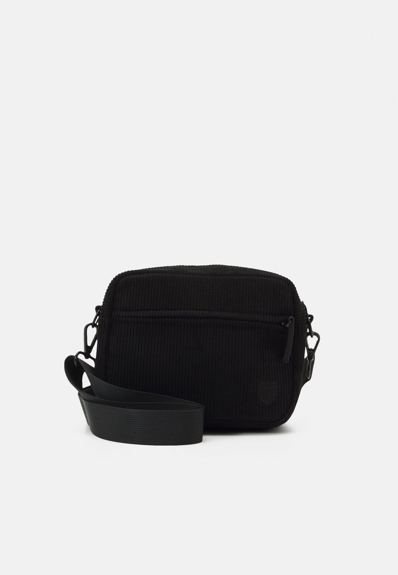 Black corduroy crossbody bag with a single zipper compartment, adjustable strap, and a textured surface. Features a subtle logo.