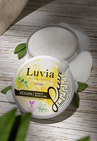 Luvia Citro vegansminkborsts-tvål, rund, silverdosan med en citron-design, skumbubblor och gröna blad på en träyta.