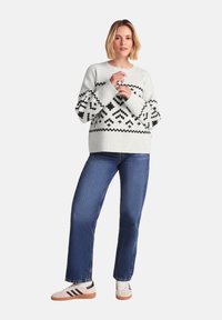 Light gray knitted sweater with black geometric patterns, paired with blue straight-leg jeans and white sneakers with black stripes.