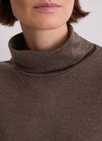 Bruine coltrui gemaakt van zachte, textuurrijke stof; aansluitend met een hoge kraag en subtiele stikdetails.