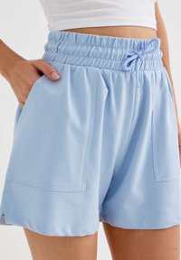 Pantalones cortos de algodón azul claro con cintura elástica, detalle de cordón y bolsillos laterales. Presenta un corte relajado y dobladillo redondeado.