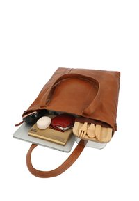 Bruine leren tote tas open, met daarin een laptop, een houten bestekset, een notitieboekje, een brillenkoker, een stuk zeep en een haarborstel.