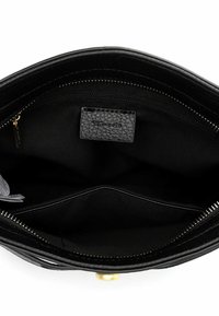Wnętrze czarnej skórzanej torebki z zamykaną na suwak przegrodą, z teksturowaną metką i gładkim wykończeniem wnętrza. Widoczne są złote elementy metalowe.