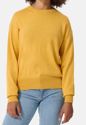 Geel gebreide trui met een ronde hals, geribbelde manchetten en onderrand. Glad textuur, losse pasvorm en drop shoulder ontwerp. Draagt bij lichte blauwe spijkerbroek.
