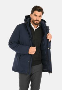 Giacca puffer blu navy con cappuccio, dotata di una zip frontale, due tasche laterali e un interno trapuntato. Il tessuto sembra liscio e resistente.