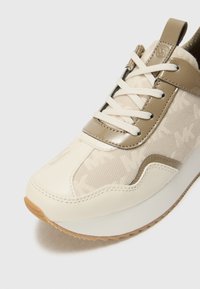Sneaker met een beige en crème textiel bovenwerk, gladde lakaccenten en een stevige rubberen zool. Veters in het wit met een logodetail op de tong.