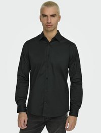 Zwarte langlopende blouse van gladde stof met een puntkraag, knoopsluiting aan de voorkant en een getailleerd ontwerp, gecombineerd met donkere jeans.