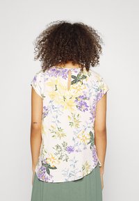 Bloemenblouse met korte mouwen van lichtroze stof met gele en paarse bloemen, ronde halslijn, detail met sleutellochting aan de achterkant en een gebogen zoom.
