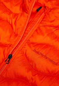 Giacca isolante di un vivace arancione, con texture trapuntata, una cerniera nera e il logo ricamato "Peak Performance" sul davanti.