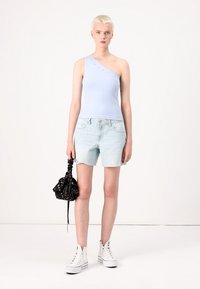 Top azul claro de um ombro só com detalhes, combinado com calções de ganga claros e uma bolsa preta com estampado floral e cordão. Ténis brancos de cano alto.