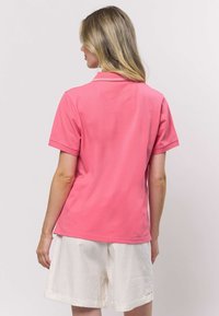 Ružové polokošeľa s krátkymi rukávmi, vybavená klasickým golierom a hladkou, textúrovanou látkou, kombinovaná s bielymi šortkami.