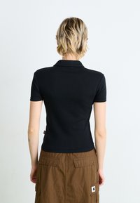 Camisola polo preta de manga curta com gola, com um design ajustado e estilo minimalista. Combinada com uma saia cargo castanha até ao joelho.