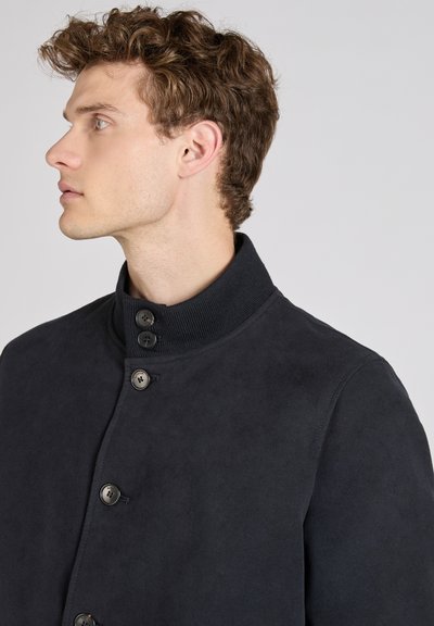 Donker marineblauwe jas van gestructureerde stof met een hoge kraag, vier knopen en een eenvoudig, modern ontwerp. Vlotte afwerking zonder patronen.