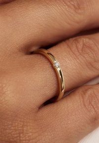 Gold band ring featuring a polished finish and a small diamond accent. Worn on a hand with textured skin, displaying a simple design.