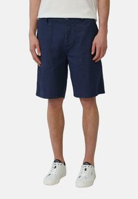 Donkerblauwe katoenen shorts met zakken, lichtgewicht stof, rechte pijp, gedragen met witte sneakers en een eenvoudige witte t-shirt.
