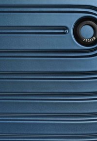 Maleta rígida de color azul oscuro con una superficie texturizada, que cuenta con estrías horizontales y un acento de hardware circular negro con la etiqueta "JASLEN."