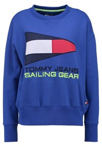 Modrá mikina s kulatým výstřihem, s velkým grafikou plachetnice v červené, bílé a námořnické modré. Obsahuje text "TOMMY JEANS SAILING GEAR" v neonově zelené barvě.
