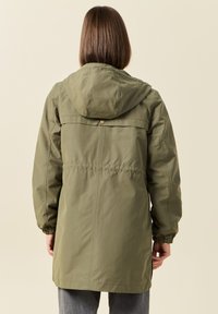 Veste parka vert olive avec capuche, poignets élastiques, coutures avant et arrière, et un accent en bouton près du col. Texture de tissu lisse.