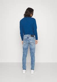 Modrá košile s dlouhým rukávem spárovaná s džínami světle modré barvy. Džíny mají hladkou texturu a standardní design s pěti kapsami.