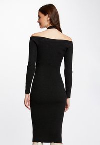Zwarte geribbelde gebreide jurk met een off-the-shoulder ontwerp, lange mouwen en een aansluitende silhouet, tot halverwege de kuit. Minimalistische stijl.
