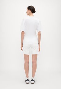 Hvit kortermet skjorte og hvite shorts, kombinert med hvite og svarte sneakers. Enkel, jevn tekstur med en skreddersydd passform.