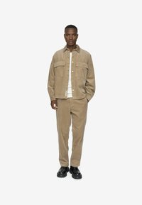 Brun kordfløjljakke med to frontlommer, parret med matchende kordfløjl bukser. Sorte sko fuldender outfittet. Enkel, afslappet design.