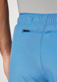 Calções de desporto azuis com um tecido texturizado, apresentando perfurações para respirabilidade e um pequeno bolso com fecho atrás.