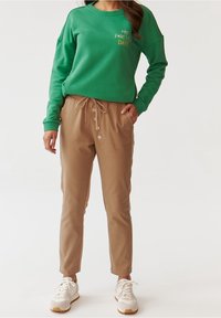 Zielona bluza z napisem "MY FOREVER DATE", zestawiona z beżowymi spodniami zwężanymi u dołu, z talią na sznurek i guzikami. Całość dopełniają białe trampki.