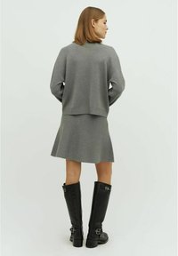 Grijze gebreide trui met verlaagde schouders, gecombineerd met een grijze uitlopende mini-jurk. Model draagt kniehoge zwarte leren laarzen met gespspecifiek.
