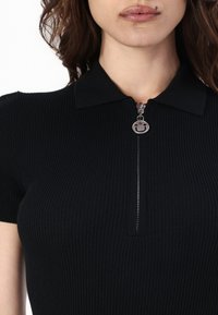 Black ribbed polo shirt with short sleeves, featuring a zippered front with a round smiley face pull tab.