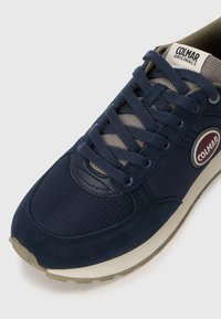 Navy blue sneaker featuring mesh and suede materials, round toe, lace-up design, and a prominent logo patch on the side.
