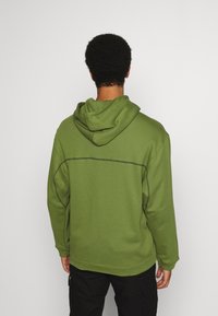 Grön huvtröja med strukturerad yta, justerbar huva och kontrasterande sömmar. Har en avslappnad passform och långa ärmar.
