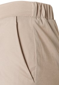 Beige pants with an elastic waistband and a side pocket, showing fabric texture and stitching details.