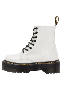 Botas de combate de cuero blanco con cordones negros, suela gruesa de goma negra y detalle de costura amarilla a lo largo del borde de la suela.