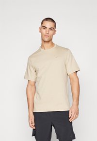 T-shirt à manches courtes col rond beige en tissu doux, avec un petit logo Nike en beige plus foncé sur la poitrine gauche.