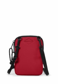Borsa in nylon rossa a forma rettangolare, con tracolla nera regolabile e chiusura a zip. Presenta un piccolo dettaglio embossato sulla parte anteriore.