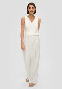 Biała bluzka bez rękawów z kwiatowym haftem, zestawiona z luźnymi białymi spodniami o wysokim stanie i delikatnym połysku.