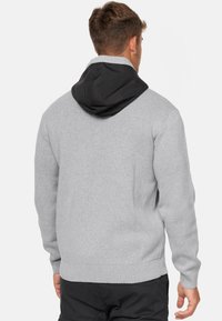Sweat à capuche gris avec une capuche noire. Texture en tricot doux, poignets et ourlet côtelés. Présente un design fonctionnel et une coupe décontractée.