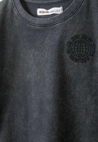 Mörkgrå bomullströja med rundad halsringning och broderad jordglob-logotyp med texten "Sedan 1987" på vänster bröst.