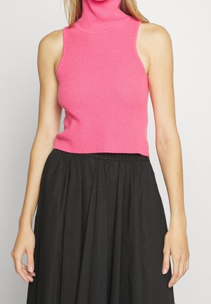 Haut sans manches rose côtelé à col montant, associé à une jupe noire froncée taille haute, porté par une personne debout.