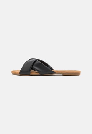 Sort lædersandal med en snoet stropdesign. Glat tekstur, åben tå og flad korksål. Minimalistisk stil.