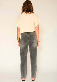 T-shirt ample beige clair avec manches tombantes, associée à un jean en denim gris délavé taille haute avec poches arrière et jambes droites.