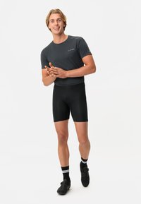 Pantaloni sportivi neri e una t-shirt grigia aderente, entrambi realizzati in materiale elasticizzato e traspirante, con scarpe da ciclismo nere e calzini a righe.