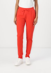 Röda joggingbyxor av mjukt tyg med elastisk midja och dragband. Avsmalnande ben, sidofickor, bärs med vita sneakers.