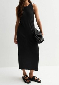 Robe maxi noire à côtes avec un design sans manches, assortie à un sac à main noir texturé et des sandales plates noires.